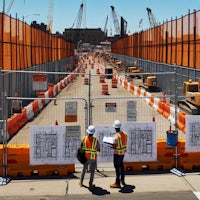 two construction workers standing in front of an orange barrier